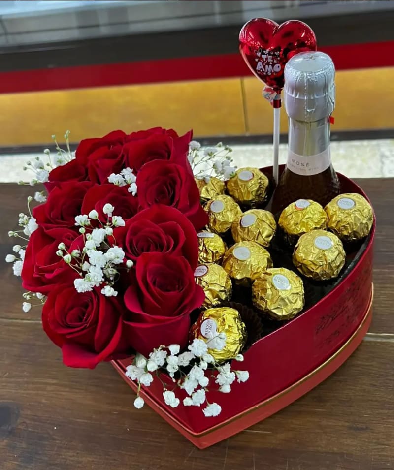 Caja floral en forma de corazón con rosas rojas, bombones Ferrero Rocher y una botella de espumoso